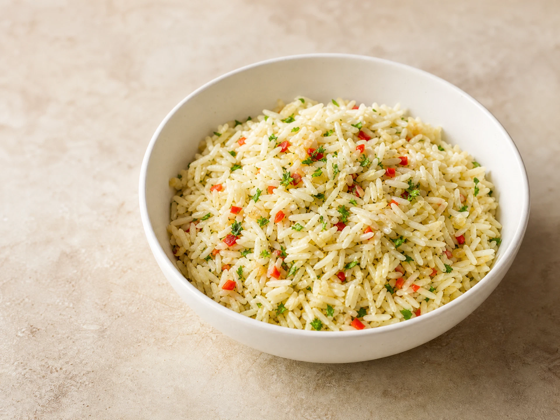 Arroz temperado com alho, cebola, ervas e pequenos pedaços de pimentão em tigela clara.