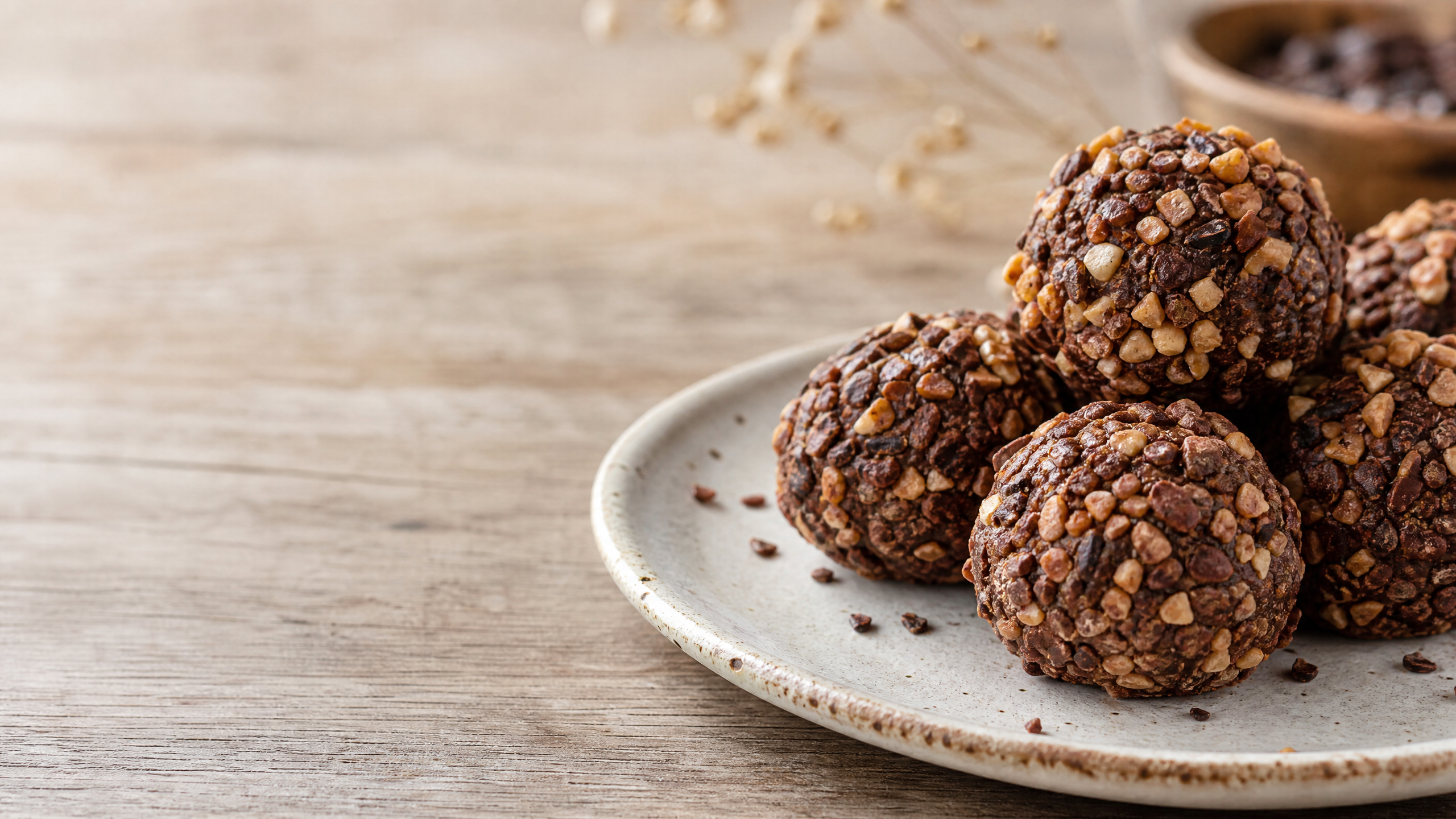 Close-up de brigadeiros gourmet enrolados e cobertos com pedaços crocantes de amendoim torrado dispostos em forminhas de papel sobre uma mesa de madeira rústica.