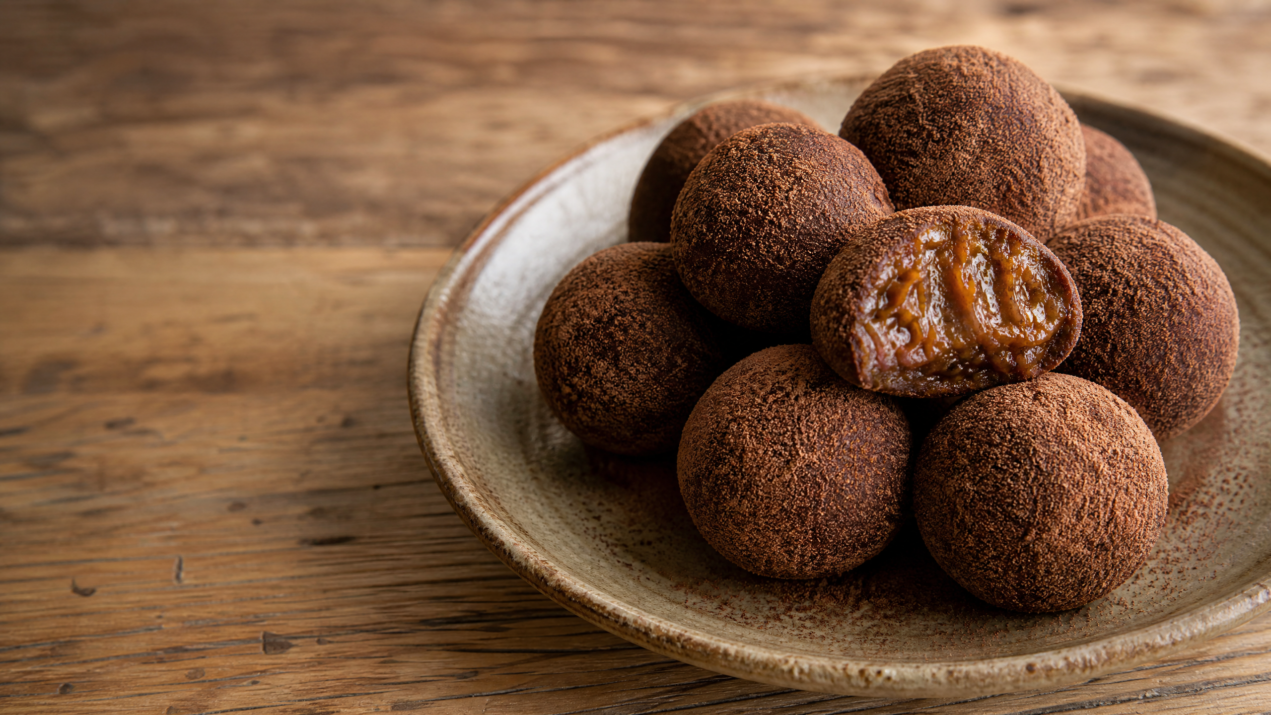 Close-up de uma porção cremosa de brigadeiro de banana em tigela cerâmica, polvilhado com cacau em pó e decorado com rodelas de banana fresca ao fundo, sob luz natural difusa.