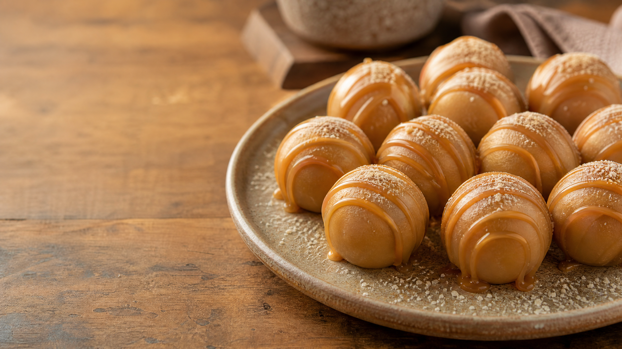 Close-up vertical de brigadeiro de caramelo cremoso em ponto de colher, polvilhado com flor de sal e servido em uma tigela rústica sobre fundo neutro de madeira.