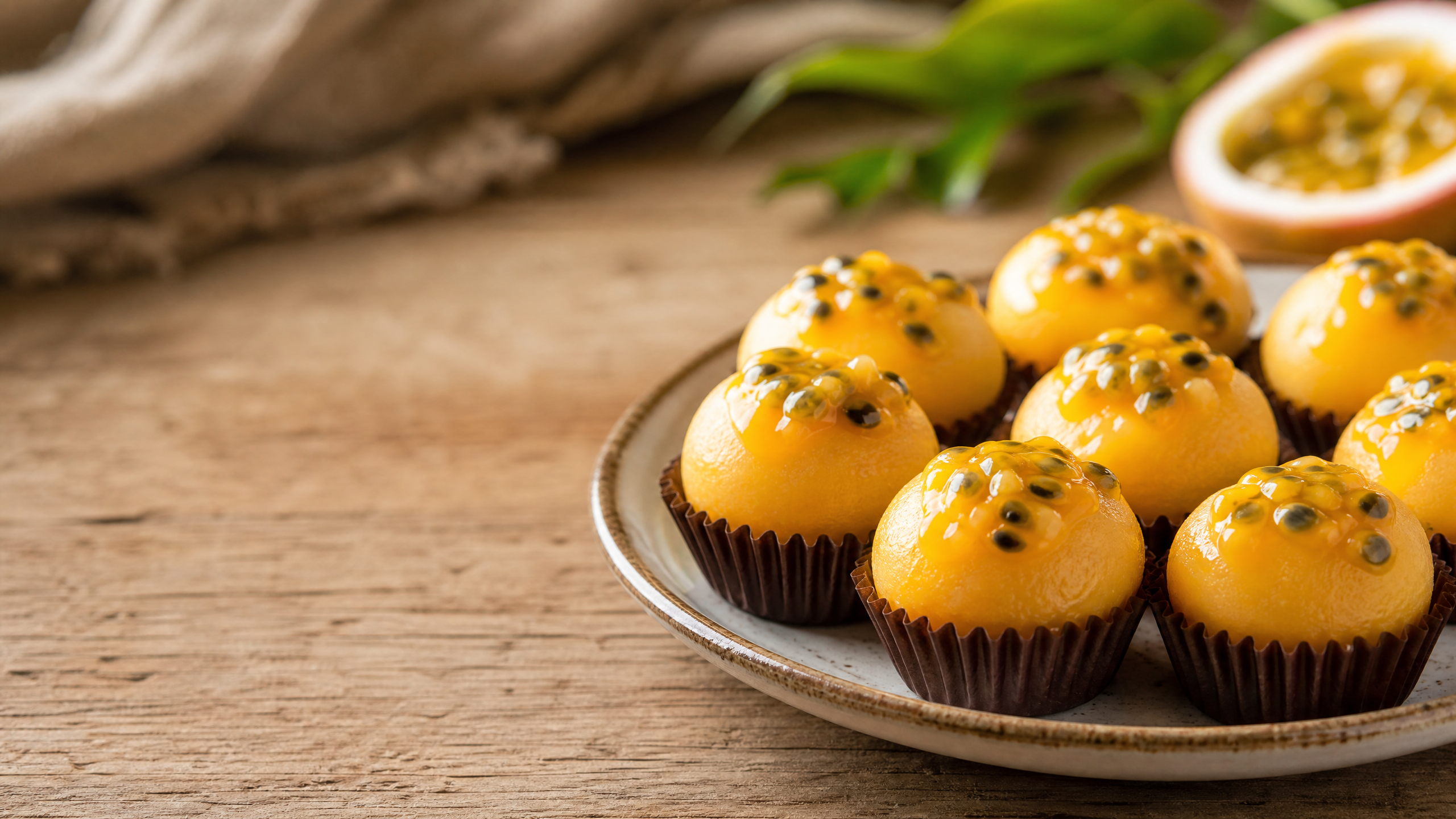 Fotografia em plano fechado de brigadeiros artesanais de maracujá enrolados, decorados com sementes frescas da fruta sobre uma superfície de madeira rústica, destacando a textura cremosa e a cor amarela vibrante.