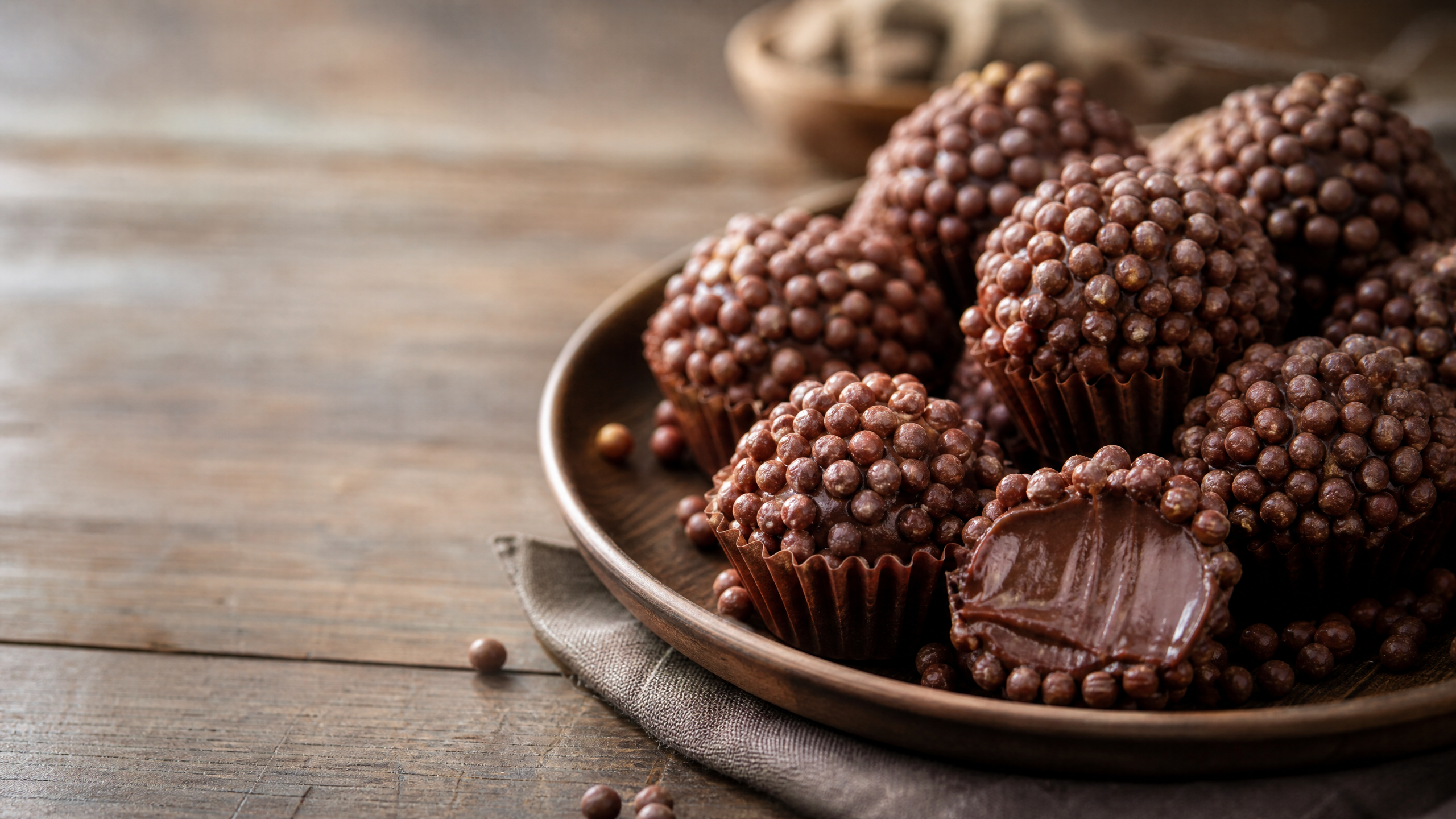 Prato com brigadeiros gourmet cobertos por flocos crocantes de Ovomaltine em fundo neutro.