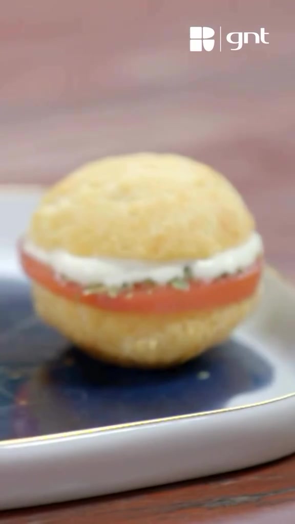 Pão de queijo recheado com tomate, creme de ricota e orégano, com marca d'água GNT preservada.