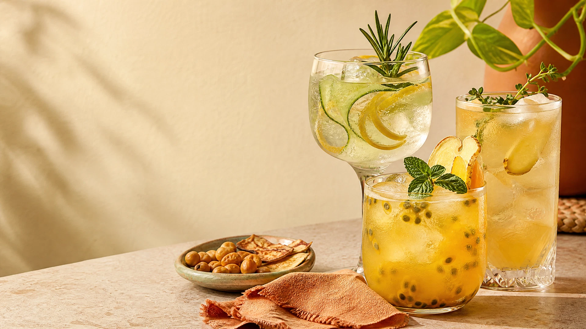 Três drinks sem álcool com cítricos, ervas, gelo e água com gás sobre bancada clara.